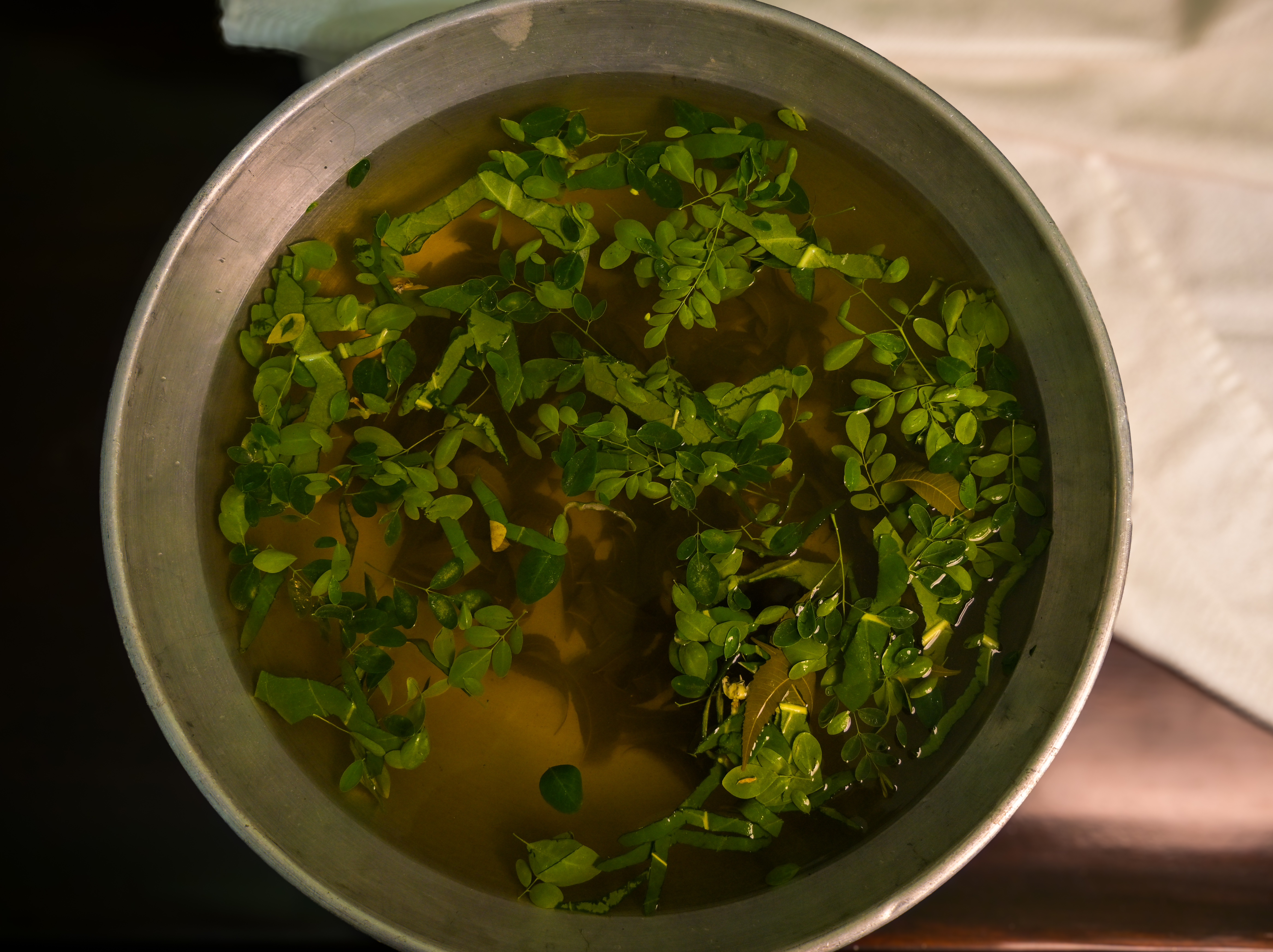 A bowl of herbal water or decoction with green leaves.