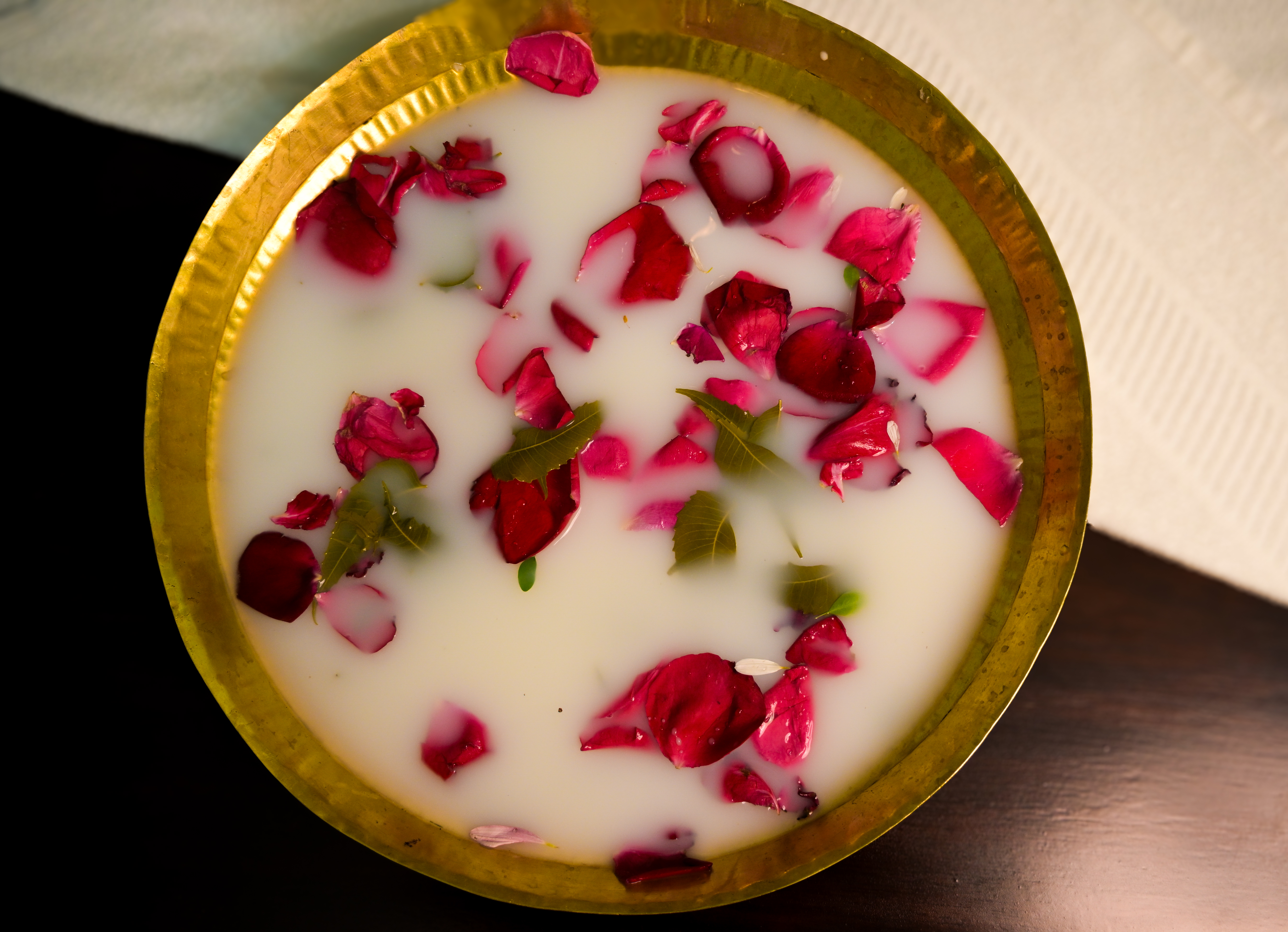 A brass bowl filled with milk and rose petals for a ritual or bath.
